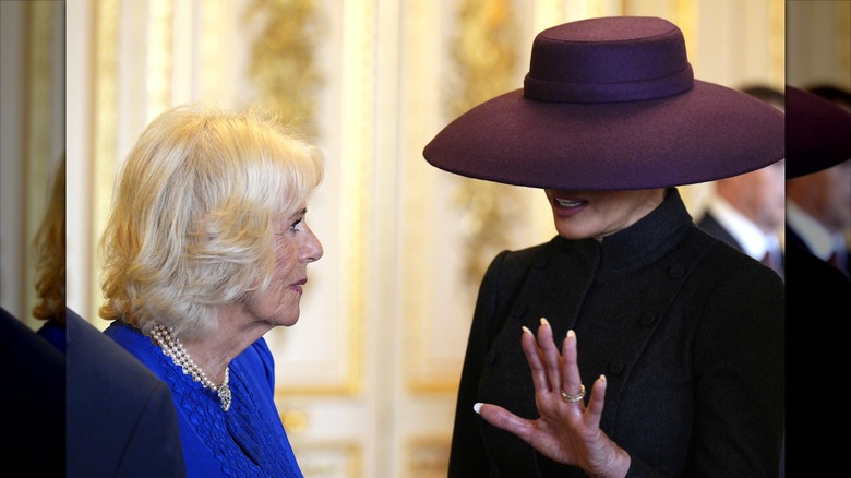 Melania Trump with her hand raised, talking to Queen Camilla.