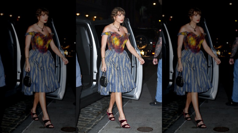 Taylor Swift stepping out of a car onto the sidewalk in a multipatterned dress.
