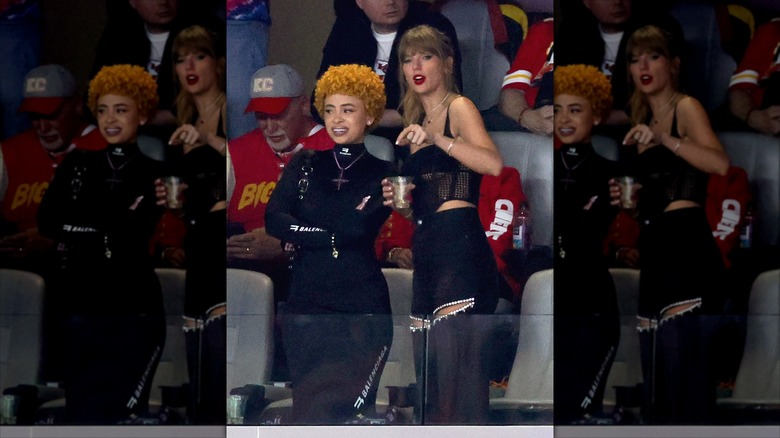Taylor Swift gesturing with a drink in hand while talking to Ice Spice.