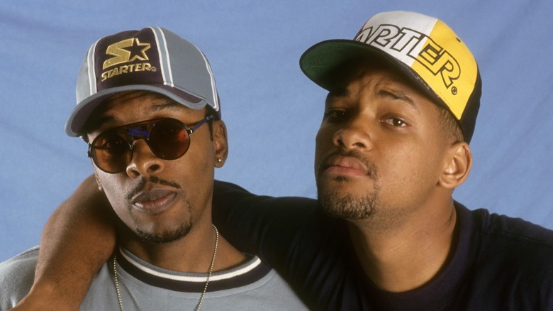 DJ Jazzy Jeff wear a grey cap and shades and a matching top next to Will Smith wearing similar cap and leaning his arm over Jeff's shoulder.