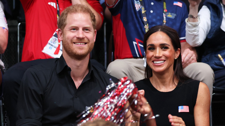 Harry and Meghan smiling while sitting together in an audience