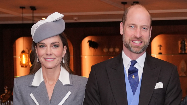 Kate Middleton wearing gray suit and hat with ribbon, Prince William wearing suit and blue vest