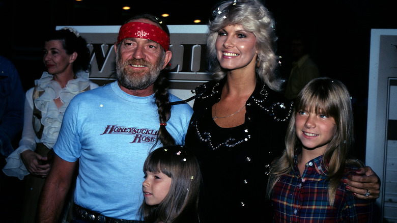 Willie Nelson wearing red bandana and blue shirt with wife and daughters