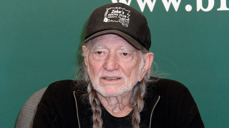 Willie Nelson wearing black baseball cap and jacket at an event
