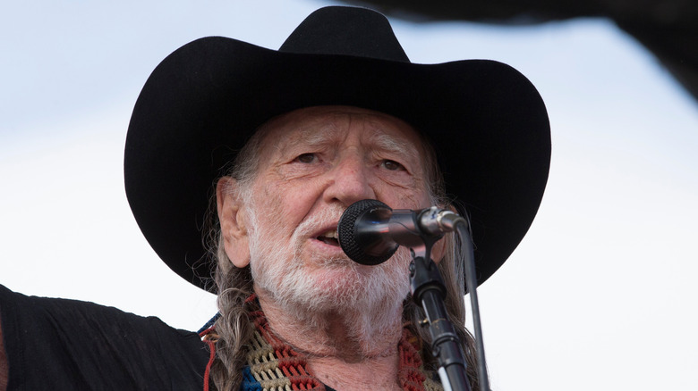 Close up of Willie Nelson in black cowboy hat singing on stage