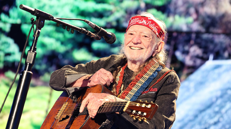 Willie Nelson wearing red bandana and brown shirt while performing on stage