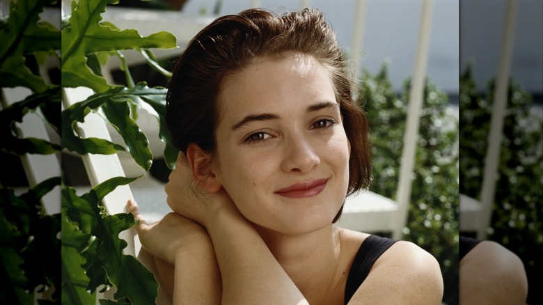 Winona Ryder smiles with her hands on her shoulder