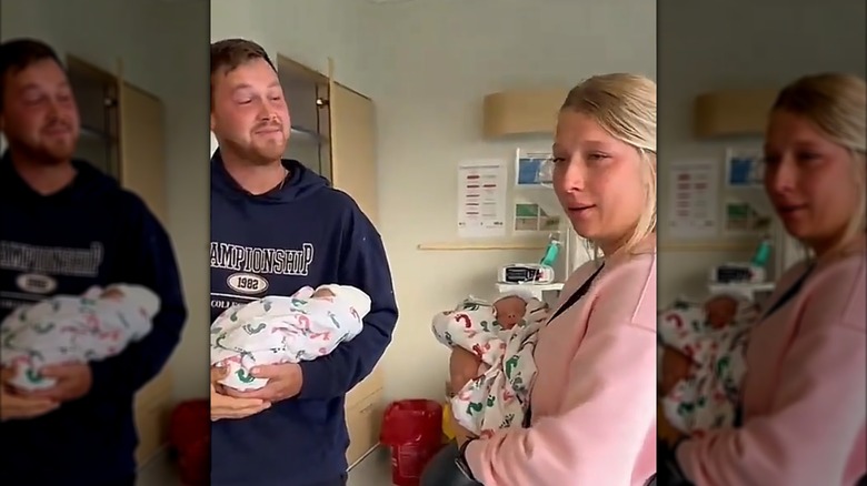 A man holding a newborn baby looking at a teary-eyed woman holding another newborn baby