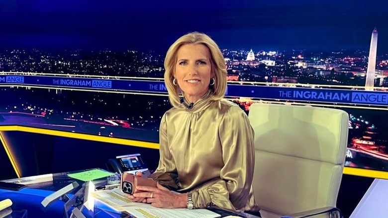 Laura Ingraham looking into the camera while sat at her studio desk with her phone in her hands