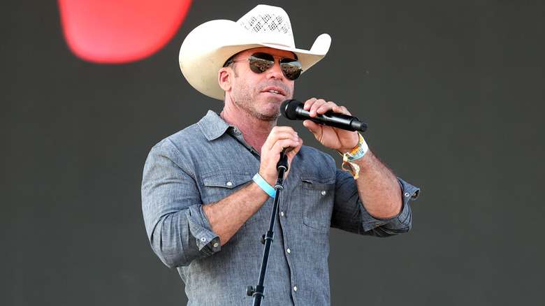 Taylor Sheridan speaking on stage at Stagecoach wearing hat and glasses