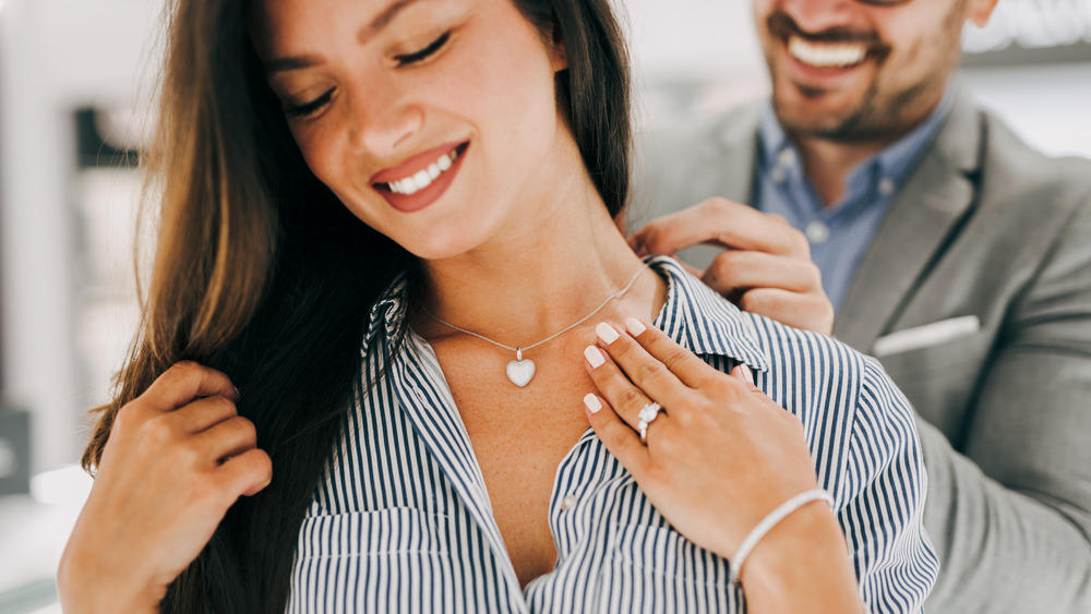 Woman smiling while a man puts a necklace on her