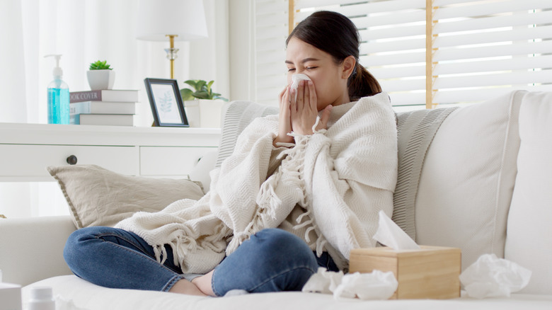 Woman blowing nose surrounded by tissues