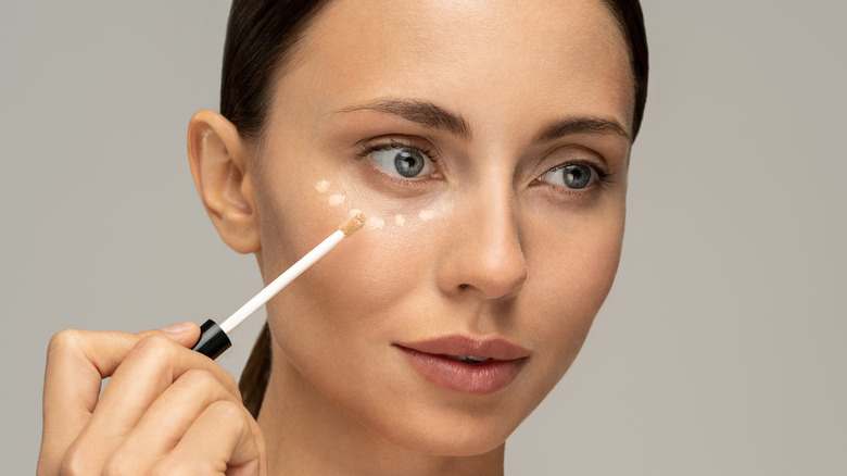 Woman applying concealer to under eyes