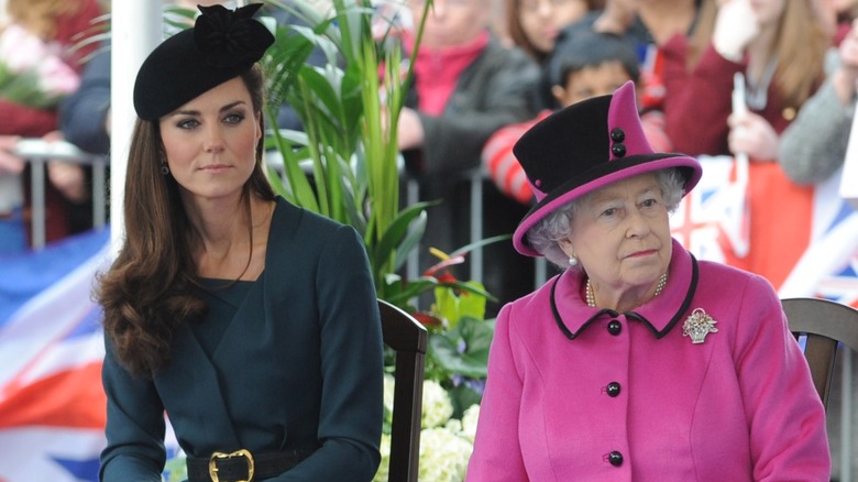 Kate Middleton sitting next to Queen Elizabeth II, both straight-faced