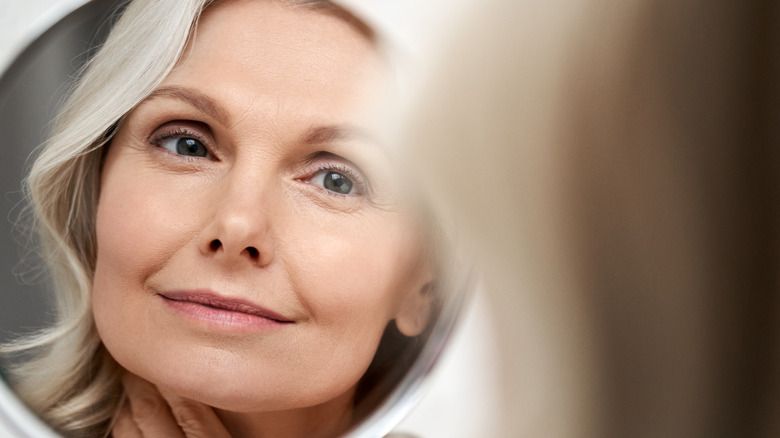 Elderly woman with gray hair looking into mirror