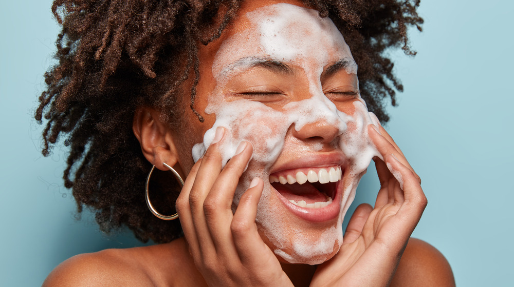 Woman smiling with suds on her face and her eyes closed.