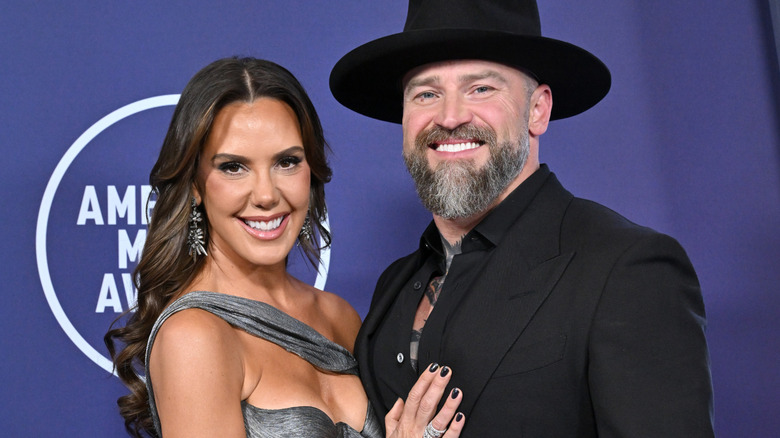 Zac Brown smiling while posing on the red carpet with Kendra Scott as she places a hand on his chest