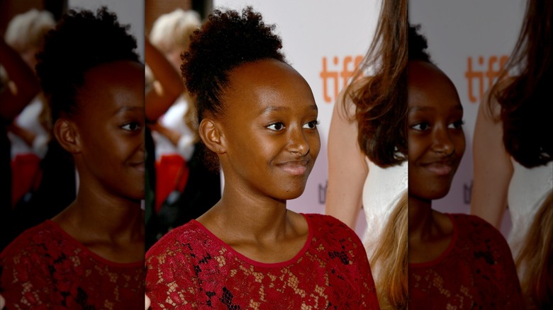 Zahara Jolie-Pitt poses in a red top with her hair in a curly ponytail