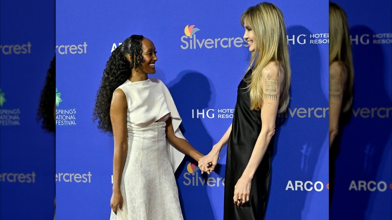 Zahara Jolie-Pitt smiles at Angelina Jolie while sporting a long, curly ponytail with side bangs