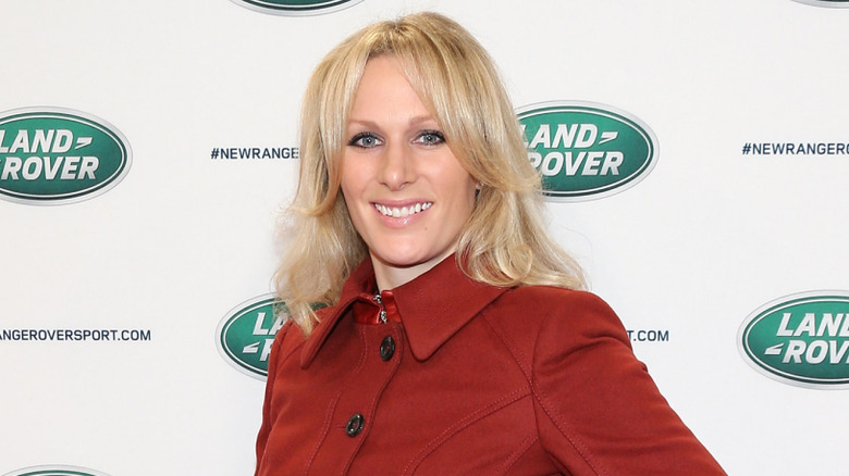 Zara Tindall posing in an orange coat with blond hair on step-and-repeat