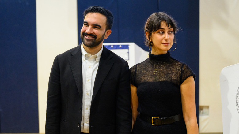 Zohran Mamdani and Rama Mamdani together in front of voting booths.