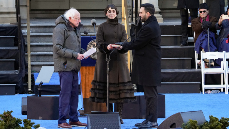Bernie Sanders, Rama Duwaji, and Zohran Mamdani standing at microphone