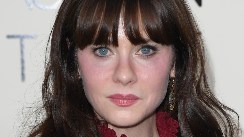 Zooey Deschanel in a black floral outfit and small golden hoops