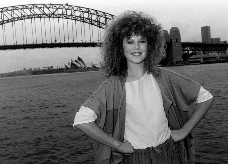 Nicole Kidman posing with her hands on her hips in front of a body of water with a bridge in the background