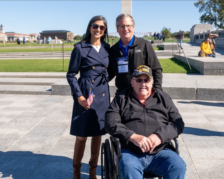 Usha Vance smiling and holding a small American flag while standing with two men