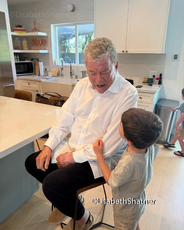 William Shatner sitting in a chair and looking down at a child