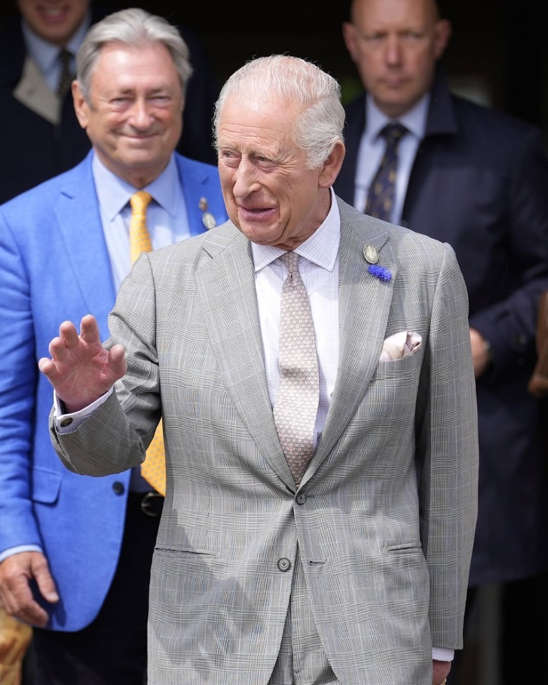 King Charles raising his hand as he walks in front of other men