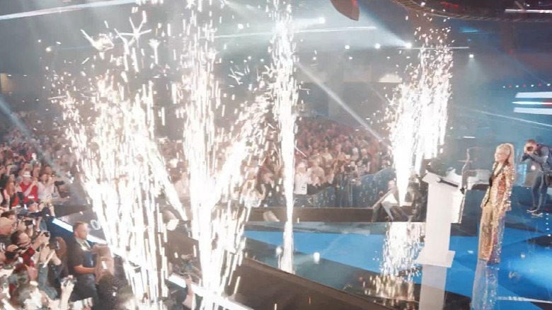 Erika Kirk on stage in her gold outfit with fireworks going off