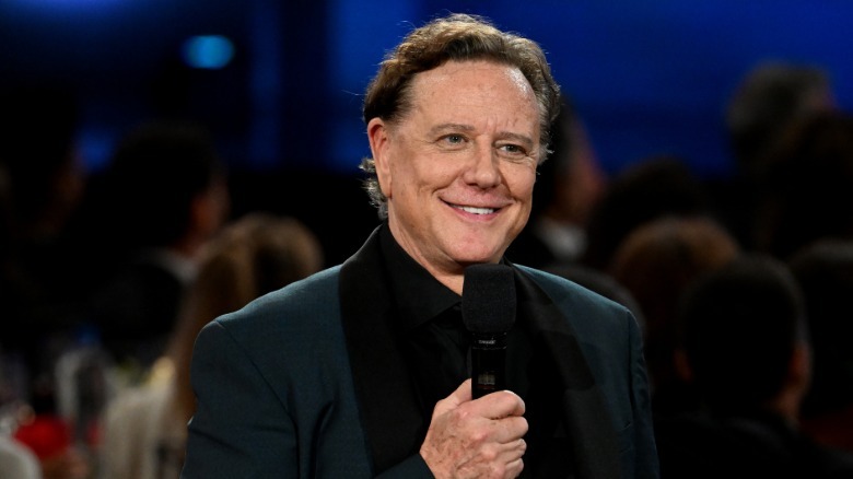 Judge Reinhold wearing a dark green tuxedo and holding a mic while smiling
