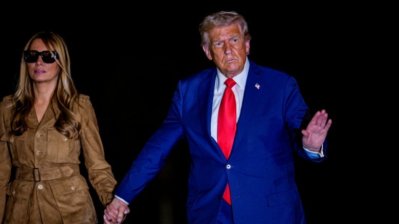 image shows Donald Trump in a blue suit holding hands with Melania Trump at night