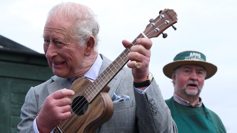 King Charles III playing a ukulele while a man stands in the background