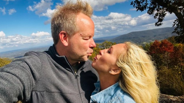 Brian Glenn and Marjorie Taylor Greene pose for a kiss with a hilltop in the background