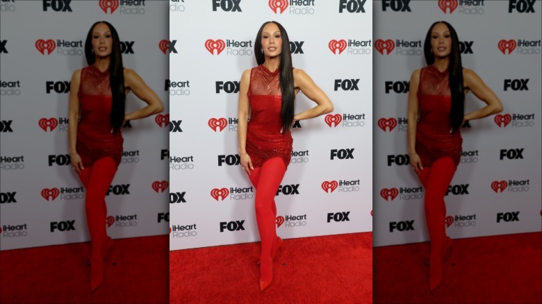 Cheryl Burke in an all-read outfit on the iHeartRadio red carpet posing with her hand on her hip