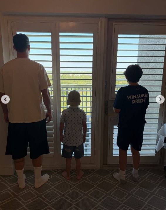 Justin Timberlake and his sons standing in front of open window shutters